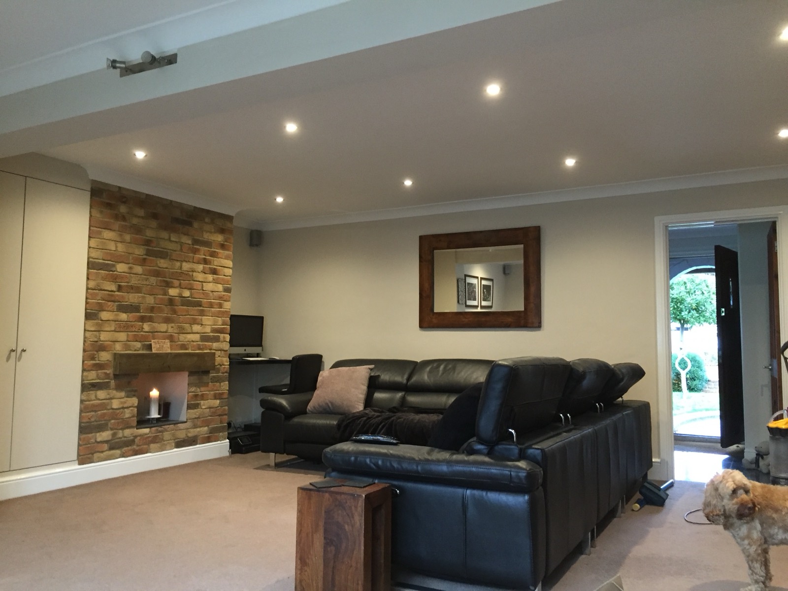 Recessed lighting across an open-plan living room, with the feature brick fireplace picked out — a whole-room lighting scheme done by Stay Safe.